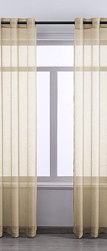 Pair of beige sheer grommet curtains hanging on a black rod in a bright living room.