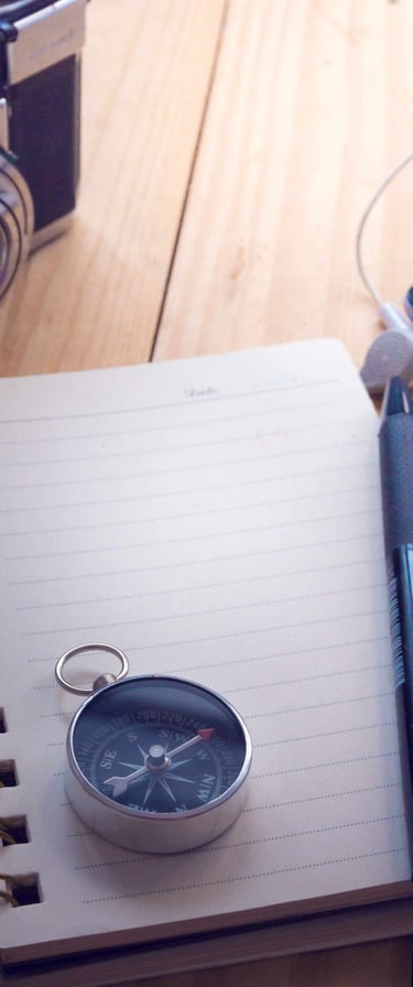 A compass on top of a notebook, with a pen and camera on the side