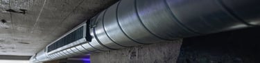 Industrial spiral ductwork and ventilation grille installed against a concrete ceiling in a modern basement.