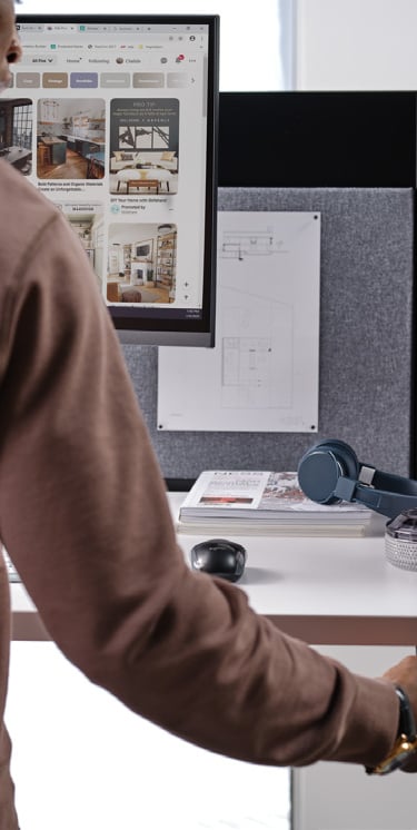 a man in a brown sweater is standing in front of a computer monitor