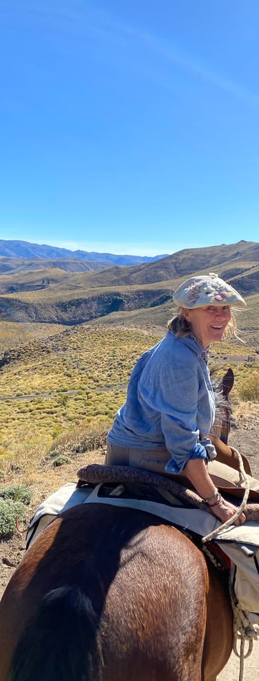 A person on a horse smiling with a mountainous landscape behind them.