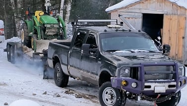 A tractor loaded on a flatbed trailer being pulled in the snow showing expertise at hauling