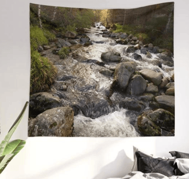 Wall tapestry on wall with autumnal river printed on it, bed in situ underneath.