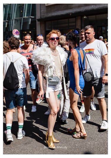 Eine Frau in einer Menschenmenge trägt eine Sonnenbrille und einen Federmantel.