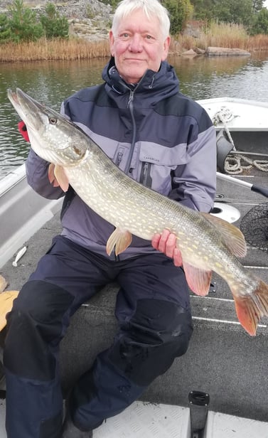 a man is sitting in a fishing boat in sweden, he caught a pike in sweden.