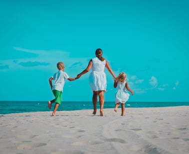a mother and her two kids walk down the beach holding hands, their backs are to us