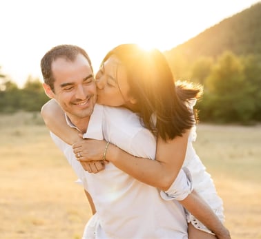 Playful couple at sunset in Provence — she rides on his back and kisses his cheek in soft light
