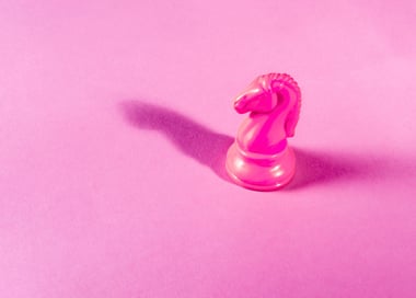 Peça de xadrez em forma de cavalo, na cor rosa, destacando-se em um tabuleiro de xadrez.