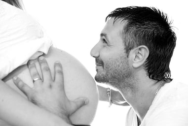 Photo de grossesse en noir et blanc, portrait du futur papa embrassant le ventre