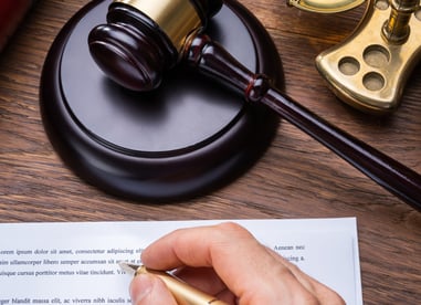 Judge's gavel sitting on a desk along with a hand holding a pen about to sign a document.