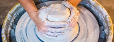 An individual's hands throwing a mound of clay on a potter's wheel.