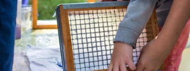 The hands of two children lifting a small screen while making paper.