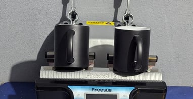 two black mugs siting on a mug press, with words below