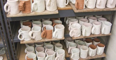 Shelves full of glazed slab mugs waiting to be fired.