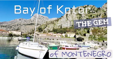 Majestic white cliffs over a bay with boats & a sign: 'Bay of Kotor: the gem of 🇲🇪 '