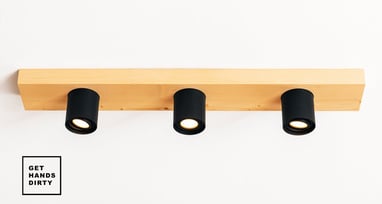 Image of a concrete ceiling with a wood block attached. The wood block has black spotlights fixtures