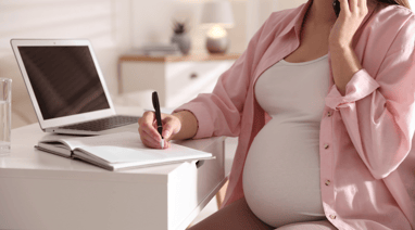 a pregnant woman sitting at a desk with a laptop and a pen