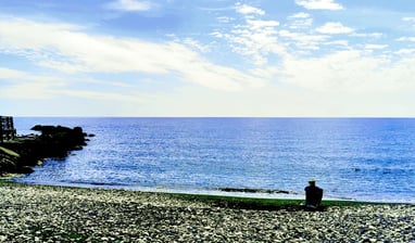 a man sitting on a rocky beach next to a beach iin Cyprus