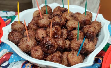 A bowl of crockpot meatballs with colorful toothpicks sticking out on a Christmas tablecloth
