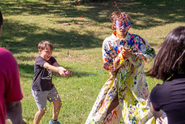 Summer Camp children shooting paint at the teacher in a white trenchcoat.