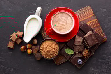 Hot chocolate in a red mug on a red saucer. Milk, chocolate squares, hazelnuts, powdered cacao, spic