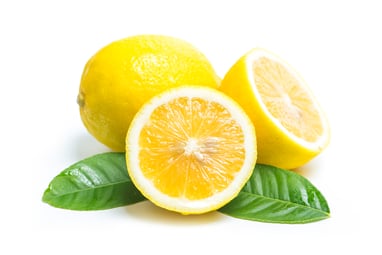 A lemon cut in half sitting on 2 leaves and a whole lemon in the white background forming a triangle