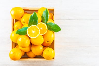 A top view of a crate filled with lemons, 1 lemon cut in half on the top of the pile and 4 leaves