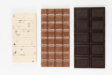 Top view of 3 chocolate bars on a white background. From left to right white, milk, & dark chocolate