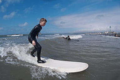 A young male surfing standing up riding a wave with sunshine and blue skies