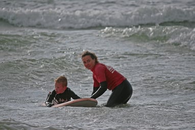 A young surfer with a female surf coach holding the board waiting for a wave