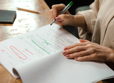 a woman in a brown shirt is writing and editing on a piece of paper