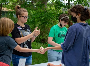 A teacher handing out balls of clay to a small group of teens.