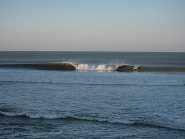 A large A frame peak, with a surfer taking off on the wave peeling to his left.