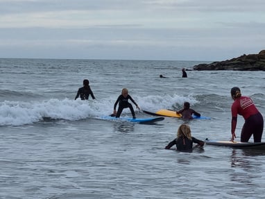 A busy after school surf club lesson with a young male surfer an a wave other children watching