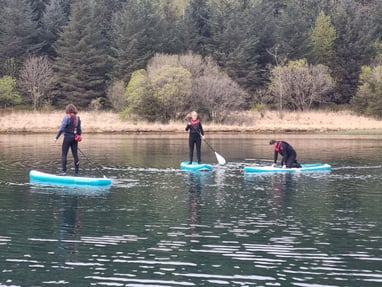 2 paddle board students and SUP coach on a calm lake.