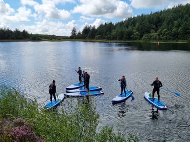 A group of paddle boarders on a calm lake surround by pine forest.