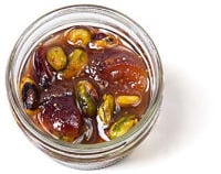 Top down view of a little, clear, open container of fig conserve with pistachio, nuts, & dried fruit
