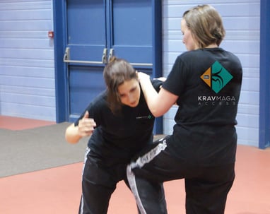 a woman in black shirt and pants standing in a room practice krav maga