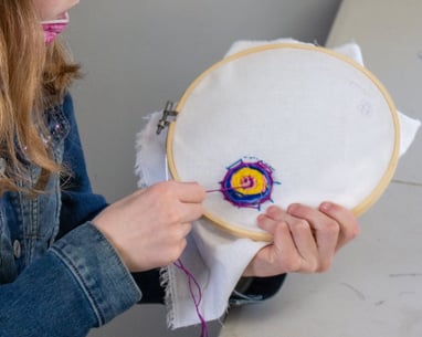 Young girl pulling thread through fabric to create an embroidered spider web.