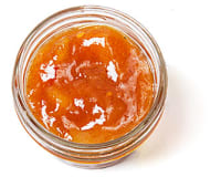 Top down view of a little, clear, open container of orange mango chutney