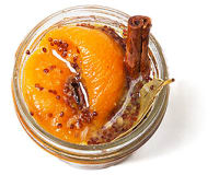 Top down view of a little, clear, open container of peach mostarda with mustard seeds & a bay leaf