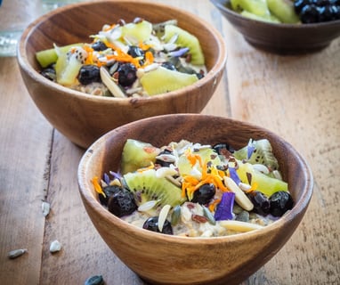 two wooden bowls of oaty chia coconut with fruit and nuts on a table