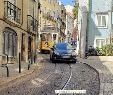 Cute yellow tram 28 follows winding tracks on a street un Lisbon