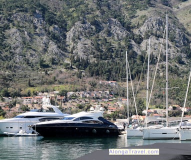 Steep white cliffs with a small town at the bottom and yachts and sail boats floating in the Bay of Kotor in front of them