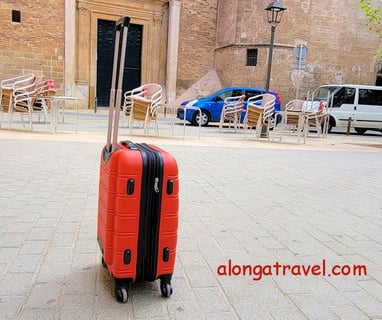 A small red carry-on standing in the middle of a square shows an ease of moving when packed light 