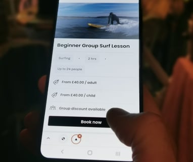 A mobile phone with a 'book now' button button visible and a thumb about to click on it.