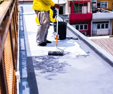 a man in a yellow jacket is painting a roof