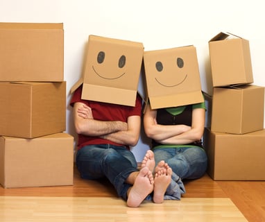 a man and woman sitting on the floor with boxes of boxes with smiley faces