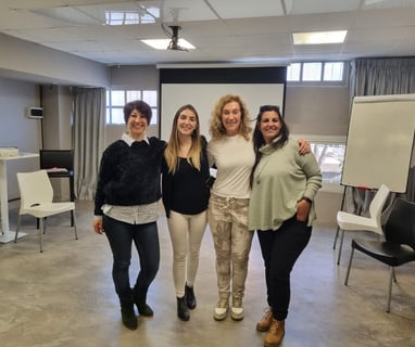 three women standing in a room with chairs and a projector