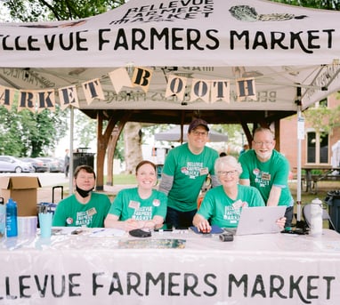 Volunteers smile from behind the Bellevue Farmers Market information booth.
